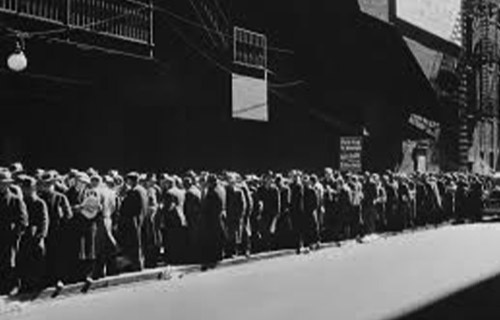 Foto em preto e branco de um cenário de 1929, em que mostra uma longa fila de pessoas, todas à calçada da rua.